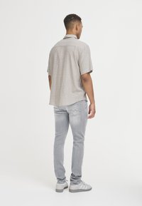 Kortärmad, rutmönstrad skjorta i beige och svart, kombinerad med ljusgrå slim-fit jeans och vita sneakers. Bakifrån visas en avslappnad passform.