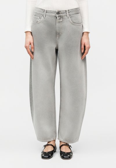 Jean gris délavé à jambes larges porté avec des chaussures plates noires ornées de clous argentés, associé à un haut blanc à manches longues côtelé.