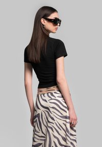 Black fitted t-shirt with short sleeves paired with a flowing beige skirt featuring a black zebra stripe pattern. Model wearing oversized sunglasses.