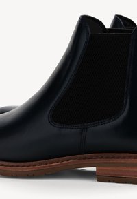 Tumesinine nahast Chelsea saapad elastsete külgpaneelidega, tekstuuriga võrgumaterjalist detailid ja pruuni kummitald. Klassikaline disain siledal viimistlusel.