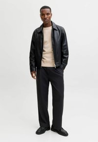 Giacca di pelle nera con chiusura a zip, maglione beige, pantaloni neri larghi e scarpe nere. Texture liscia e design moderno.