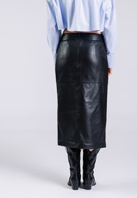 Zwarte leren midi-rok met een gladde textuur, voorzien van een split aan de achterkant en minimale naden, gecombineerd met zwarte geborduurde cowboylaarzen.