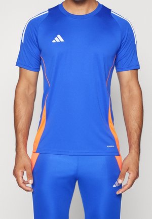 Homme portant une tenue de sport bleue avec des accents orange, haut à manches courtes avec des rayures blanches sur les épaules et pantalon assorti.