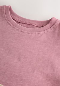 T-shirt en coton rose clair avec un col rond côtelé et une texture subtile. Le tissu semble doux et respirant, sans motifs ni imprimés.