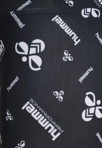 Svart atletiskt tyg med ett upprepat vitt logomönster från Hummel, med varierande logoorienteringar och storlekar över materialet.