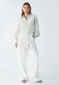 Belo širok hlače z visokim pasom, kombinirane z zeleno srajco z gumbi in črtami, z rahlo ohlapnim krojem in velikimi rokavi. Dodatki vključujejo uhančke v obliki obročev.