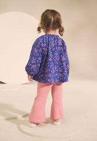Blusa blu a fiori con maniche a sbuffo abbinata a pantaloni rosa a coste svasati. Scarpe bianche completano il look.