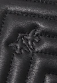 Zwart leermateriaal met een quilted ontwerp en een geperst logo. Soepele textuur met opvallende stikseldetails en een subtiele glans.