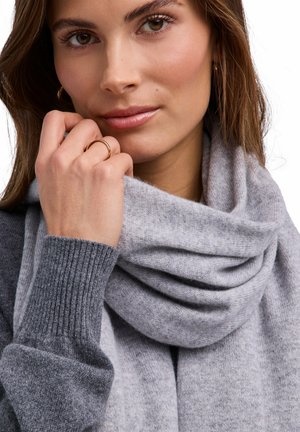 Maglione grigio lavorato a maglia con una sciarpa abbinata grigia, caratterizzati da una texture morbida. Il modello tiene la sciarpa, mostrando un aspetto accogliente e stratificato.