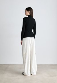 Melna ribota garām piedurknēm turtlenecka krekls, apvienots ar brīvām baltām kroku biksēm, kurām ir sānu kabatas, minimāls metāla detaļu skaits un brīva piegriezuma forma.