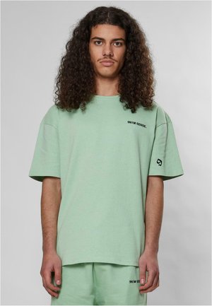 Mintgrøn kortærmet t-shirt lavet af blødt stof, med en løs pasform, rund halsudskæring og trykt logo i sort på brystet og ærmet.