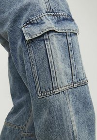 I pantaloni cargo in denim blu chiaro presentano una grande tasca a patta sul lato, cuciture visibili e una vestibilità comoda. Il tessuto ha una finitura strutturata.
