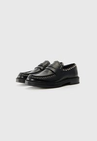 Mocassins noirs en cuir avec des détails cloutés autour du col, semelle plate et design classique. Conviennent pour des tenues formelles.
