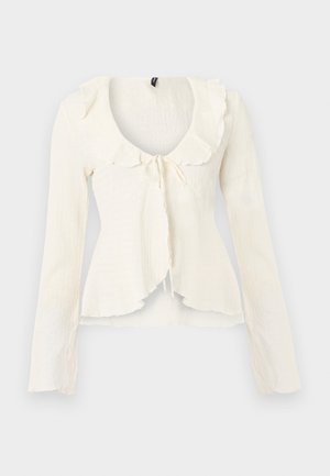 Bluza crem cu mâneci lungi, guler volanat și detaliu de legare în față, realizată dintr-un material texturat și tiv ușor evazat.