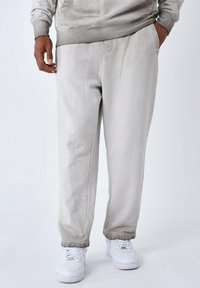 Lichtgrijze sweatpants met een relaxte pasvorm, voorzien van een gladde textuur en elastische boorden, gecombineerd met witte sneakers.