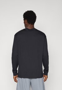 Schwarzes Langarm-T-Shirt aus Baumwolle mit Rundhalsausschnitt und lässiger Passform. Die Nahtdetails sind minimal, der Stoff wirkt weich.