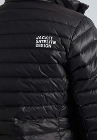 Veste matelassée noire avec piqûres horizontales, comportant le texte blanc "JACK1T SATEL1TE DES1GN" en haut du dos.