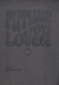 Donkergrijze stof met opgezette tekst "FUTURE LOVER" in een golvend lettertype, en een cirkelvormig logo onderaan met "FUTURE" in reliëf.