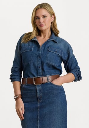 Denimskjorte med knappeåpning, to frontlommer og oppbrettede ermer, kombinert med et brunt lærbelte og denimskjørt.