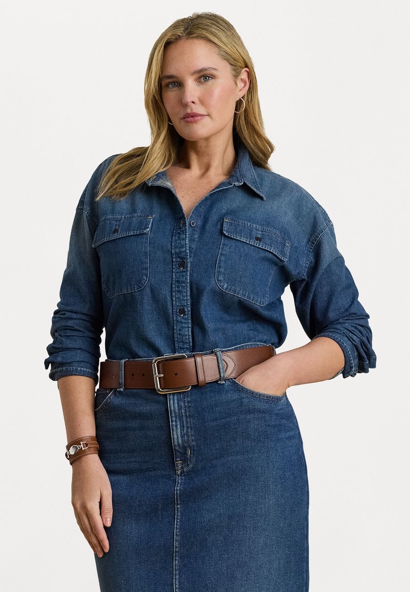 Denimskjorte med knappeåpning, to frontlommer og oppbrettede ermer, kombinert med et brunt lærbelte og denimskjørt.
