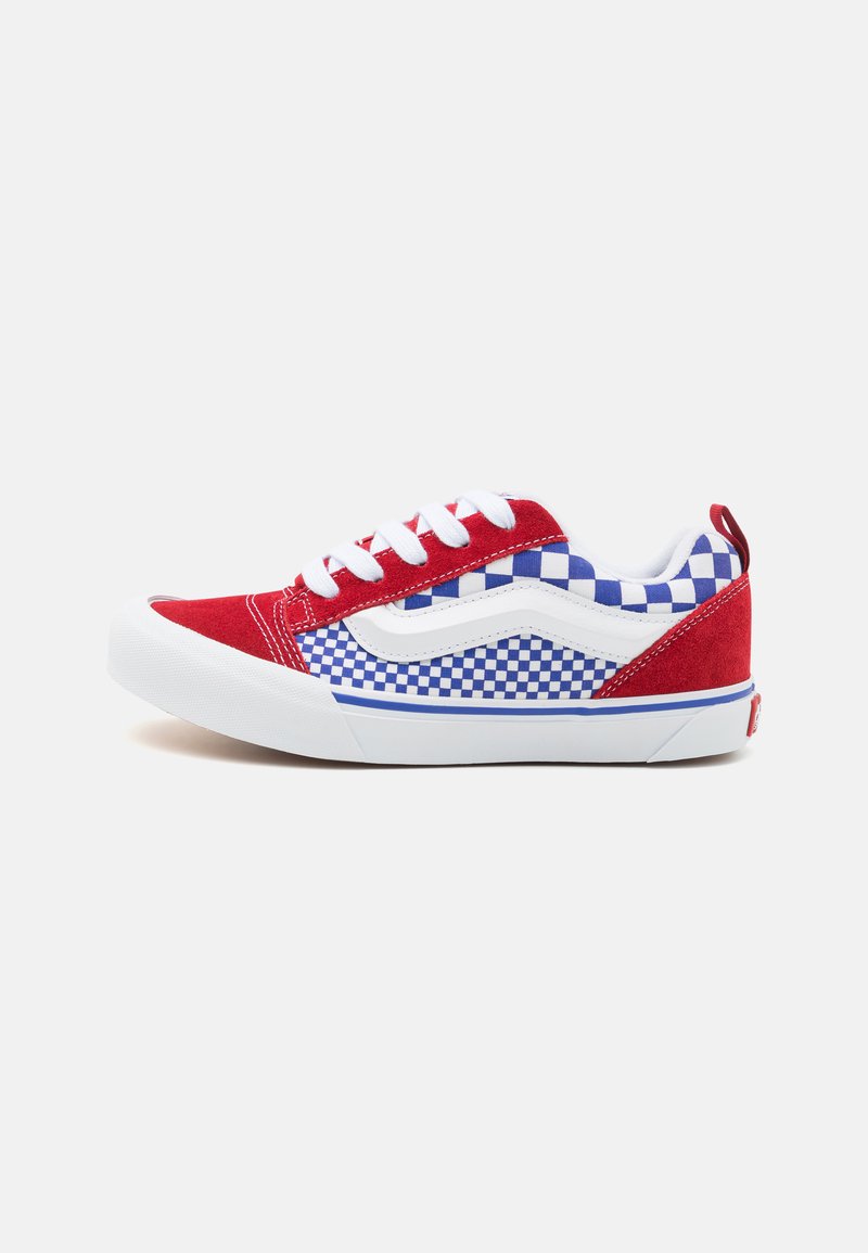 Sneaker rosso in suede con lacci bianchi, con un motivo a scacchi blu e bianchi sul lato e una suola in gomma bianca.