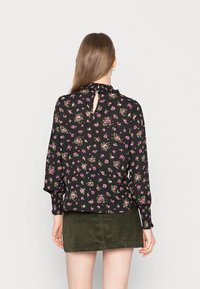 Blusa preta floral com decote em volta rufado, mangas longas e design de costas com abertura em forma de lágrima, apresentando pequenos padrões de flores rosa e verdes.