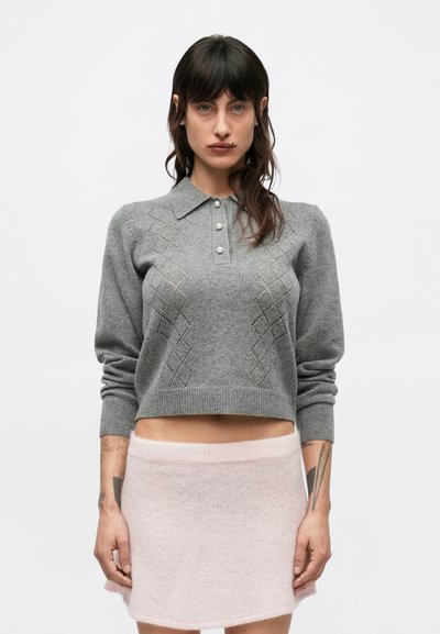 Grauer, kürzer geschnittener Pullover mit Kragen und Rautenmuster, kombiniert mit einem weichen, kurzen, flauschigen Rock in zartem Rosa, der einen breiten Bund aufweist.
