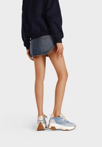 Sneaker chunky blu con suole bianche, caratterizzate da una tomaia testurizzata e un design con lacci. Abbinate a una gonna di jeans, che mostrano un look casual.