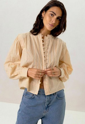 Peach-colored, button-up shirt with vertical stripes, high collar, and puffed long sleeves, made of lightweight fabric.