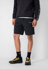 Pantaloni corti neri realizzati in tessuto leggero, con una tasca zip, cintura elastica e logo Champion. Abbinati a sneaker nere e gialle.