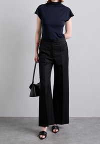 Mörkblå åtsittande topp, högmidjade svarta vida byxor, svart handväska och svarta halksandaler. Slät tyg med minimal detaljering.