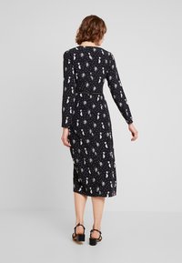 Černé dlouhé šaty s přiléhavým trupem a zvonovou midi sukní, které mají bílé vzory nebeských motivů po celém povrchu.