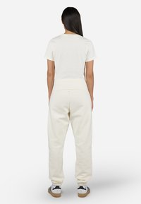 Hvit bomulls t-skjorte og kremfargede joggebukser. Løs passform, med elastisk midje og mansjetter. Støttende, flate sømmer, kombinert med sneakers.