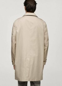 Beige trenchcoat med skräddarsydd passform, bakslits och bred krage. Tillverkad av en slät tyg med knäppta manschetter och minimal detaljering.