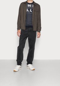 Hnědá košelová košile přes modrý svetr s motivem sobů, doplněná černými džíny a bílými teniskami s oranžovými akcenty.