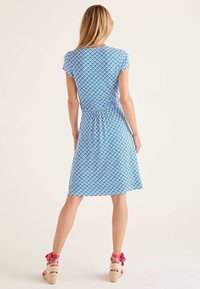 Blå mönstrad klänning med vågmönster, korta ärmar och upptagen midja, kombinerad med sandaler med remmar.