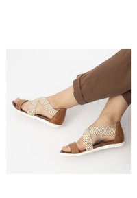 Hnědé kožené sandály s tkanými krémovými pásky se vzorem, otevřenou špičkou a bílou gumovou podrážkou. Výška podpatku je nízká.