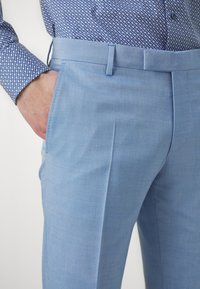 Svijetloplave hlače izrađene od glatke tkanine. Karakteristike uključuju bočne džepove i ravni kroj s elegantnim fitom i vidljivim plisiranim detaljima.