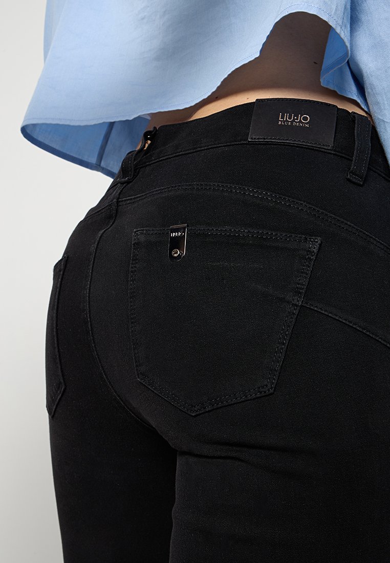 Czarne dżinsy o slim fit z przeszywaną tylną kieszenią i małą metalową metką. Połączone z jasnoniebieską bluzką.