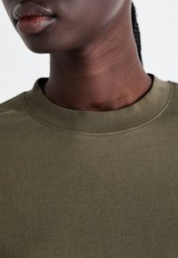 Olijf groene katoenen T-shirt met een geribbelde ronde halslijn, een gladde textuur en subtiele stiksels langs de kraag.