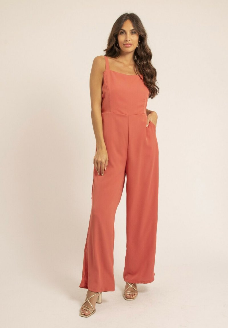 Combinaison en coral avec bretelles fines, jambes larges et poches latérales. Fabriquée à partir d'un tissu doux, avec une silhouette décontractée et des coutures minimales.