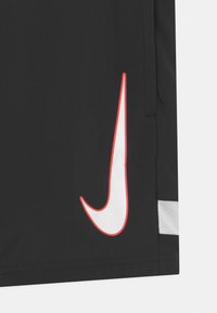 Pantalones cortos deportivos negros con un Swoosh blanco de Nike bordeado en rojo en el lado izquierdo, y un detalle de malla texturizada en el dobladillo.