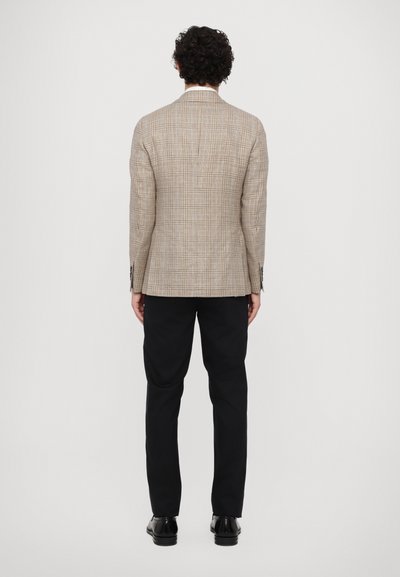 Braun kariertes Blazer mit taillierter Passform, ausgestattet mit einem geschlitzten Rücken und schwarzen Hosen, kombiniert mit schwarzen Lederschuhen.