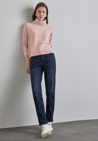 Ljust rosa texturerad polokragetröja med ribbat avslut, i kombination med mörkblå raka jeans och vita sneakers. Enkel, modern design.