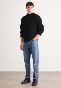 Black ribbed sweater, blue straight-leg jeans, and black sneakers. The sweater features a high neckline, and the jeans have a classic denim texture.
