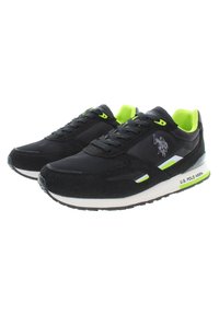 Scarpe da ginnastica nere con un esterno in rete e suede, dettagli in neon verde e una suola intermedia bianca con un logo e strisce.
