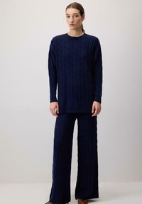 Jūras spēku zila adīta džemperis un saskaņotas bikses, piedāvājot teksturētu dizainu un ribotas piedurknes, kas nodrošina komfortablu, brīvu piegriezumu.