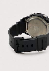 Czarny pasek sportowy do zegarka wykonany z silikonu o matowym wykończeniu, z regulowaną sprzączką na bolce oraz wieloma otworami do dopasowania rozmiaru. Tył koperty wykonany z metalowego srebra.