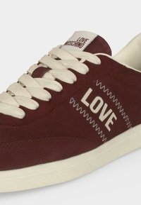 Baskets bordeaux avec lacets et semelle blancs, "LOVE" imprimé sur le côté, et "LOVE MOSCHINO" sur l'étiquette de la languette.