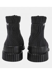 Bottes noires tricotées avec un design montante, une texture côtelée et des semelles en caoutchouc épaisses et rainurées pour la traction et le soutien.